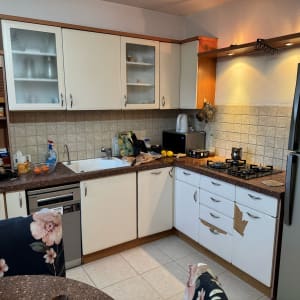 מטבח עם ארונות לבנים, כיריים ומקרר אפור