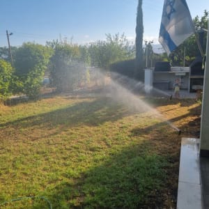 השקיית גינה עם דשא ירוק ודגל ישראל ברקע