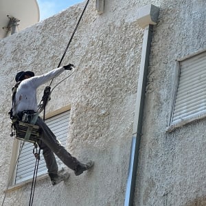 אדם עובד בגובה על קיר בניין עם חבלים