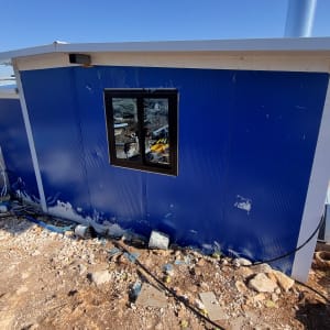 קיר כחול עם חלון, צינורות וחומרי איטום על הקרקע