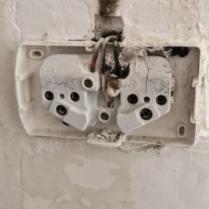 שקע חשמלי עם חוטים חשופים וקיר פגום