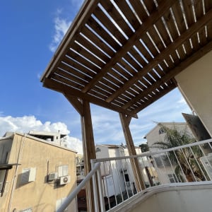 פרגולה מעץ מעל מרפסת עם מעקה לבן