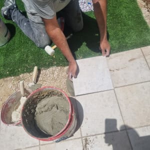 אדם מניח אריחים עם דלי מלט וכלים