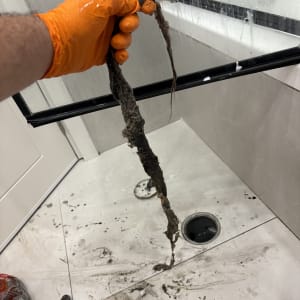 יד עם כפפה כתומה מחזיקה לכלוך שהוצא מניקוז במקלחת