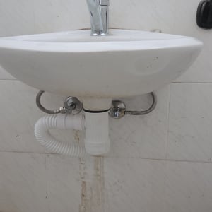 כיור עם ברז וצנרת מתחתיו על קיר לבן