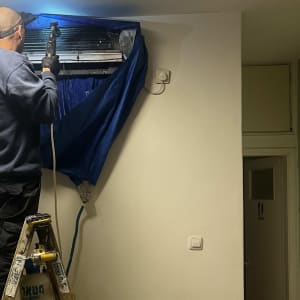 טכנאי מתקין מזגן על סולם בחדר