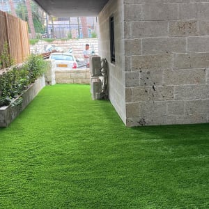 דשא סינתטי וערוגת צמחים לצד קיר אבן