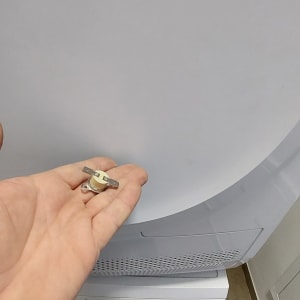 יד מחזיקה רכיב חשמלי מול מכונת כביסה