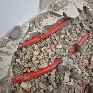 חור שנחשף בצינור מים אדום מתחת לאריחי ריצוף שבורים
