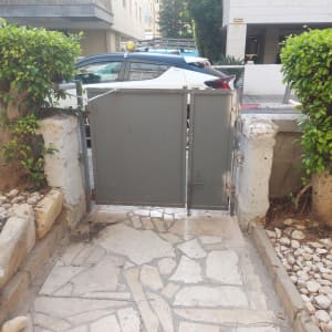 שער מתכת בין שני עצים עם שביל אבן