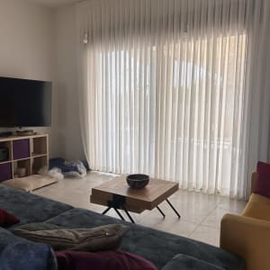 וילון לבן תלוי בסלון עם ספה ושולחן עץ