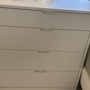 שידה לבנה עם ארבע מגירות וחוט חשמל מונח עליה