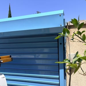 שער חשמלי כחול ליד קיר וצמחייה