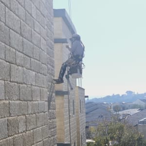 אדם תלוי על חבל מבצע עבודות גובה על קיר בניין