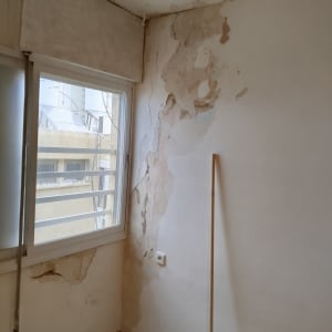 קיר עם קילופי צבע ותקרה פגומה ליד חלון
