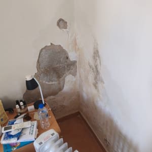 קיר עם נזקי רטיבות, שולחן עם חפצים ומנורה