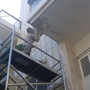 אדם עובד על תיקון קיר חיצוני עם פיגום