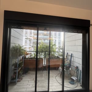 מרפסת עם צמחים וכלי גינון ליד חלון זכוכית גדול