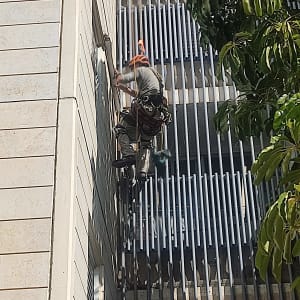 אדם עובד בגובה על בניין עם ציוד בטיחות.