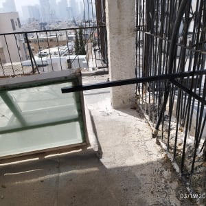 חלון זכוכית ומעקה ברזל במרפסת עם נוף עירוני