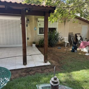 חצר עם פרגולה, שולחן עבודה וכלי גינון.