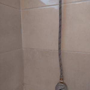 צינור מתכת עם מד לחץ מים על קיר אריחים