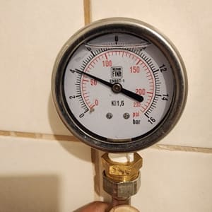 מד לחץ מים מוחזק ביד על רקע קיר