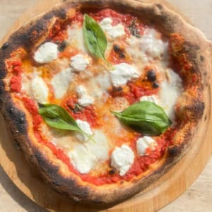 פיצה מרגריטה עם עלי בזיליקום על קרש עץ