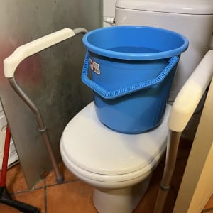 דלי כחול מלא מים על אסלה בחדר שירותים