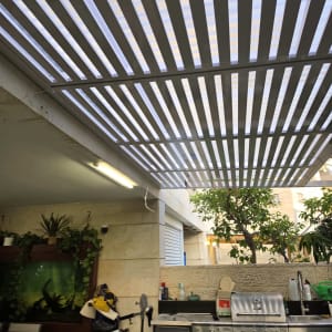 פרגולת אלומיניום לבנה עם קירוי שקוף מעל מטבח חוץ בחצר
