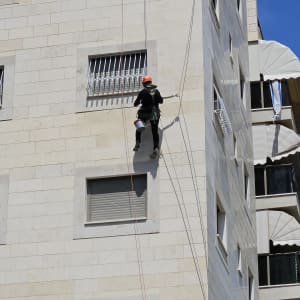 אדם עם קסדה מטפס על קיר בניין בעזרת חבלים