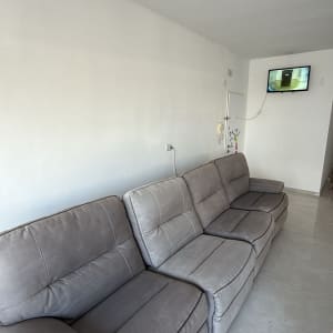 ספה אפורה בחדר עם קיר לבן וטלוויזיה תלויה