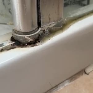 חלק תחתון של דלת מקלחת עם סימני רטיבות ועובש