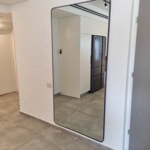 מראה גדולה על קיר בחדר עם רצפת אריחים אפורה