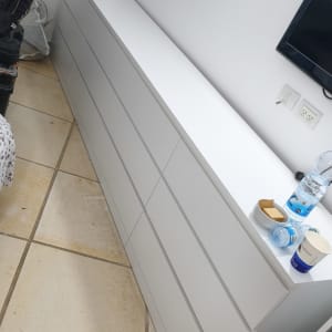 שידה לבנה עם מגירות, בקבוק מים וכוסות על השידה