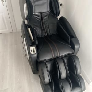 כיסא עיסוי שחור בחדר עם רצפת עץ בהירה