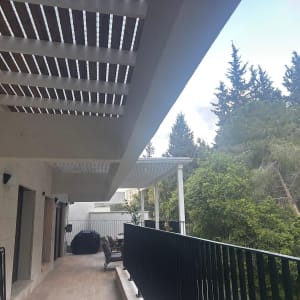 מרפסת עם פרגולה ועצים ברקע