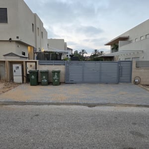 חצר עם שער וגדר, פחי אשפה ובתים ברקע