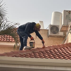 אדם צובע גג רעפים עם מברשת וצבע