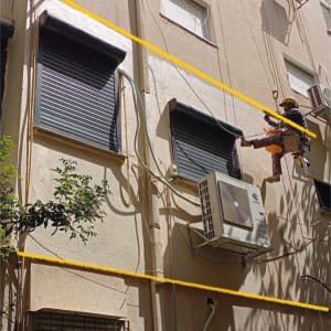 עובד בגובה מתקין מזגן על קיר חיצוני של בניין