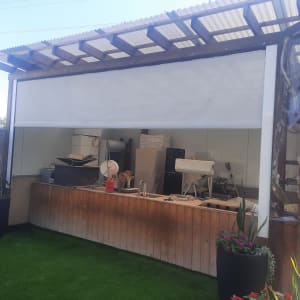 סוכך מותקן מעל אזור עבודה חיצוני עם דשא וצמחים