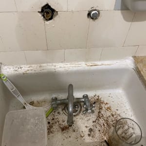 כיור עם ברז חלוד, חור בקיר, לכלוך וכלים