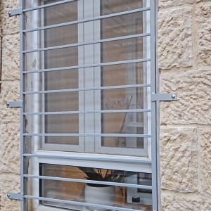 סורגי מתכת על חלון עם מסגרת לבנה