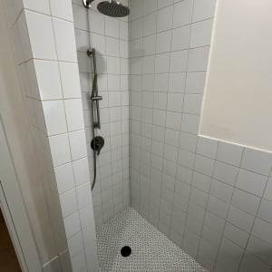 מקלחת עם אריחים לבנים וראש מקלחת מתכתי