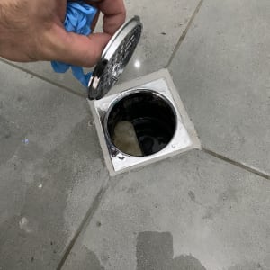 יד מחזיקה מכסה ניקוז על רצפת אריחים