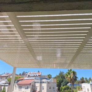 פרגולת אלומיניום לבנה עם קירוי שקוף המותקנת במרפסת גג