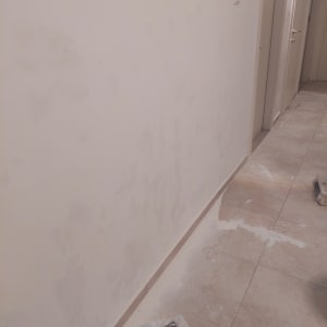 קיר צבוע עם סימני תיקון וציוד צביעה על הרצפה