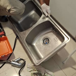 אדם מתקין כיור נירוסטה עם כלים וציוד אינסטלציה