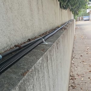 התקנת צנרת מים חיצונית עם חבקים לאורך חומת בטון בגינה