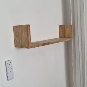 מדף עץ מותקן על קיר לבן עם שלט רחוק